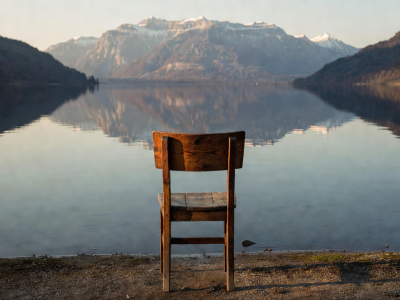 Wooden chair facing a calm lake reflecting the mountains
